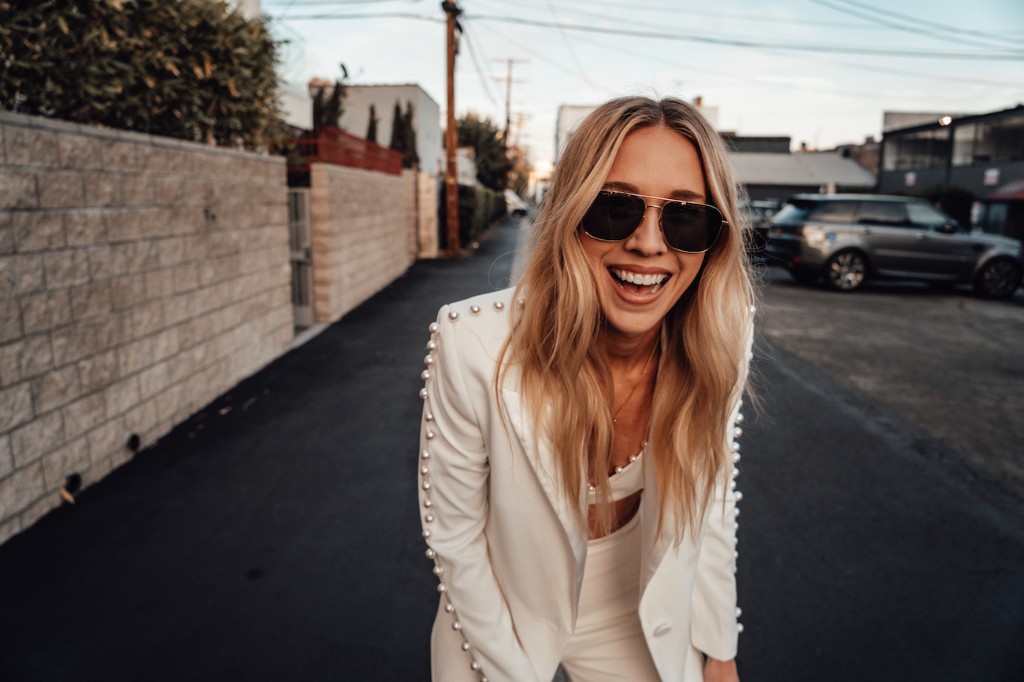Kelsey laughing on a city street in a white pearl-trim suit